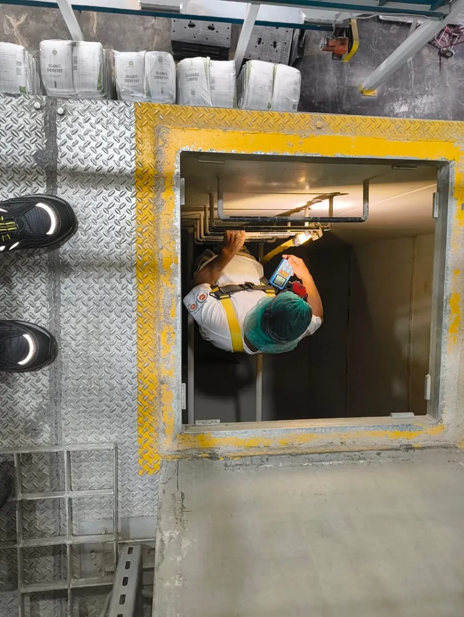 Participante con arnés desciende por una boca de acceso con un detector de gases en la mano