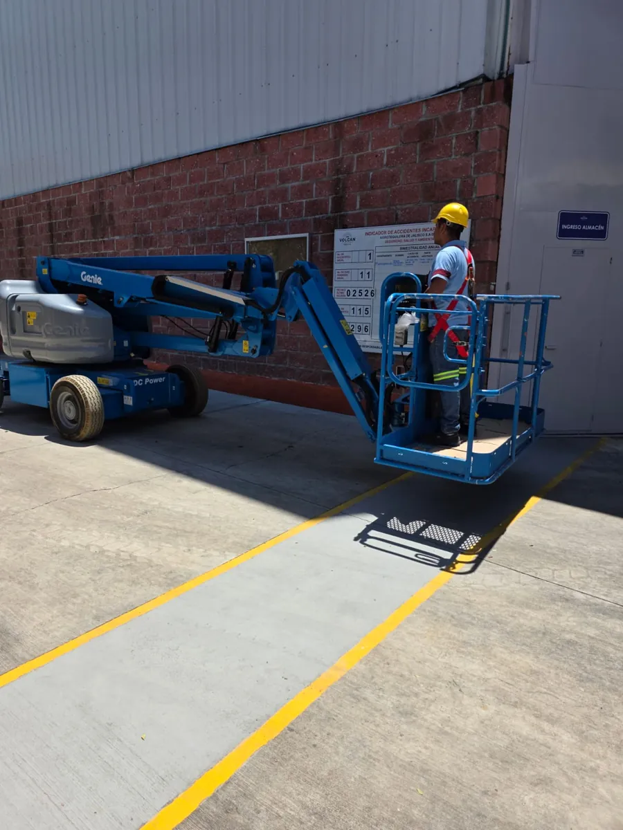 Operador con casco y arnés dentro de la canastilla de una plataforma de elevación articulada
