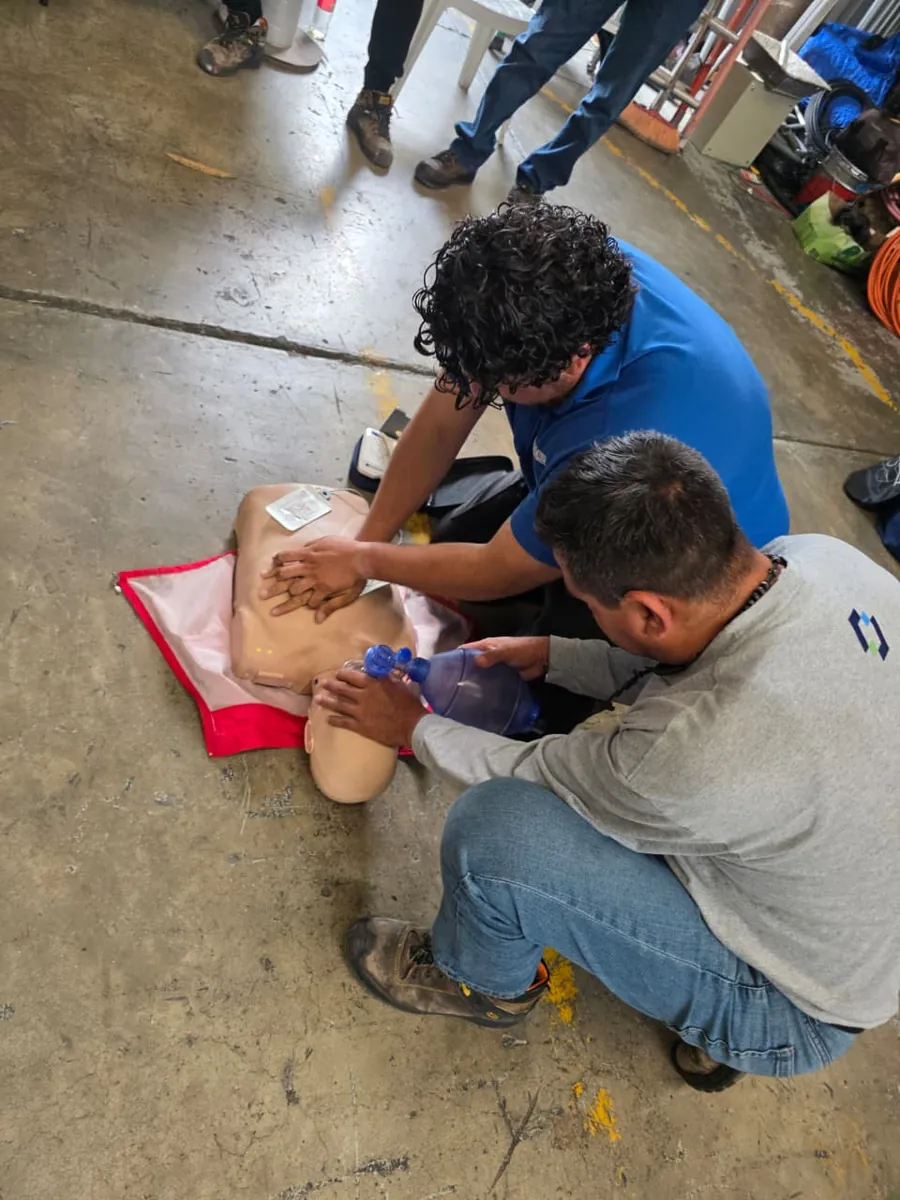 Dos participantes practican reanimación cardiopulmonar en un maniquí con bolsa de ventilación y desfibrilador