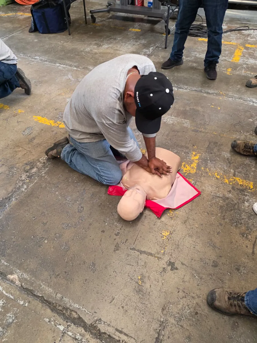 Participante arrodillado practica compresiones torácicas en un maniquí de reanimación